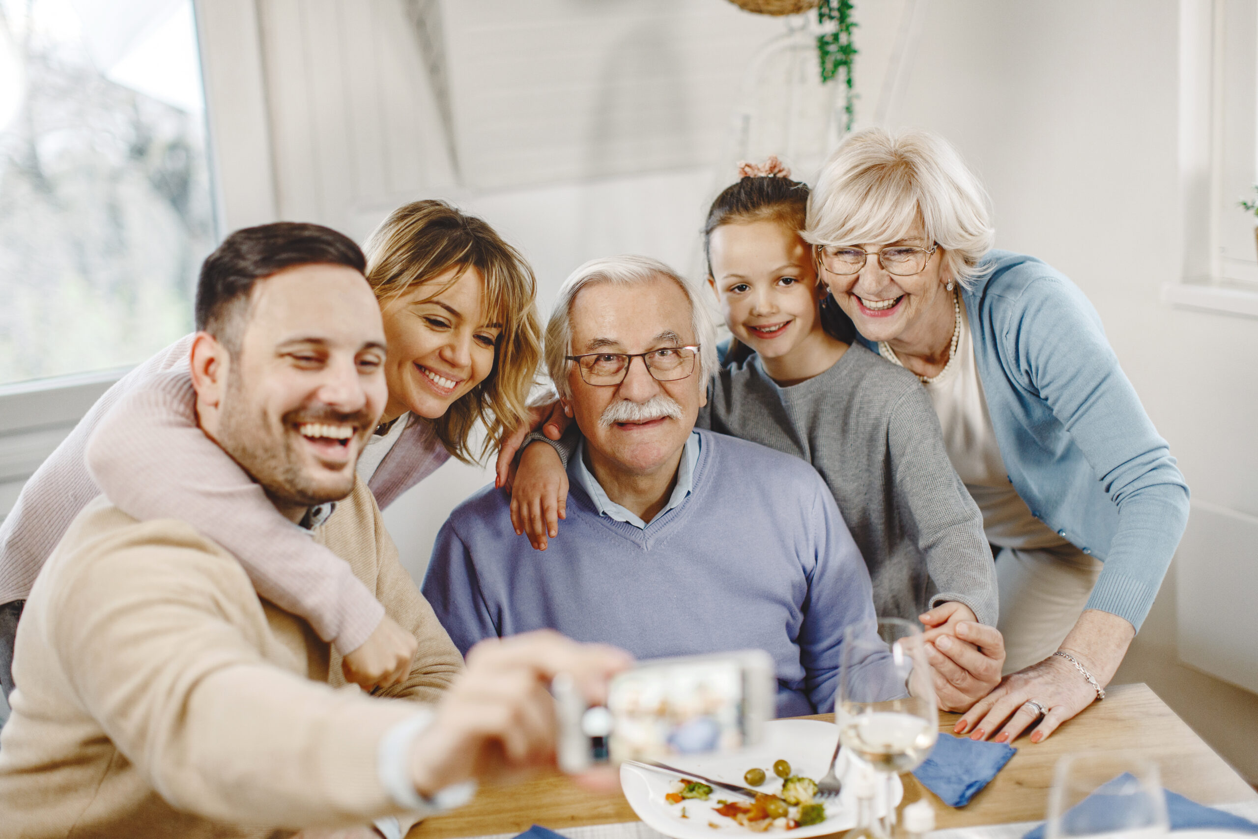 happy extended family taking selfie with mobile phone in dining room.