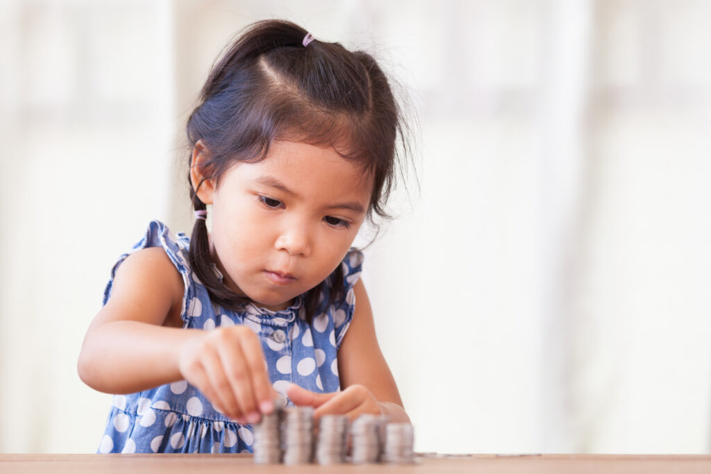 cute asian little girl playing with coins making stacks of money